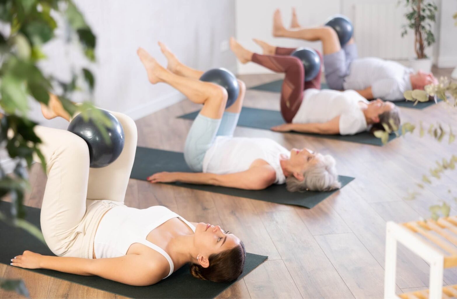 Older Women in Pilates Class with Pilates Ball Between Legs On Mats