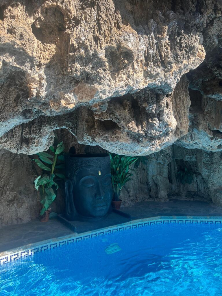 Serene Buddha statue set inside a limestone cave above the tranquil blue swimming pool at Molino del Rey retreat in Andalusia