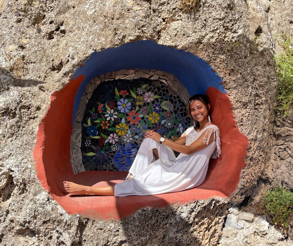 Michelle Kent sits inside a colourful mosaic alcove carved into the rock at SomaRising retreat in Andalusia, Spain, surrounded by natural textures and vibrant floral artwork
