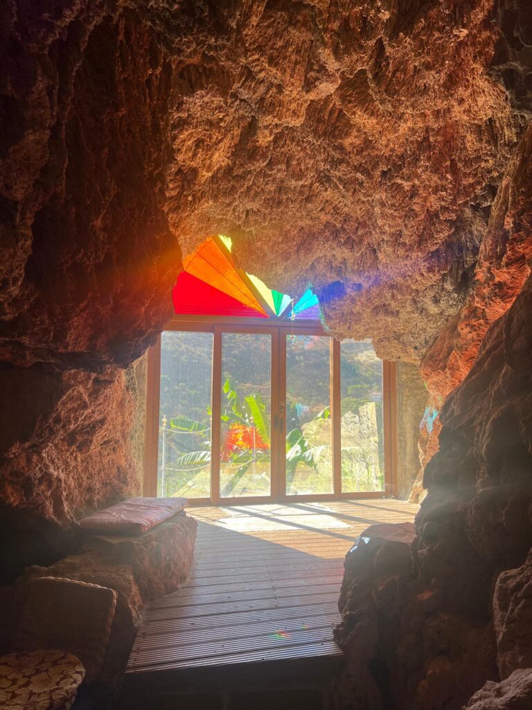 View from inside a rainbow-lit cave from coloured stained glass at Molino del Rey, overlooking the Andalusian mountains through wooden doors