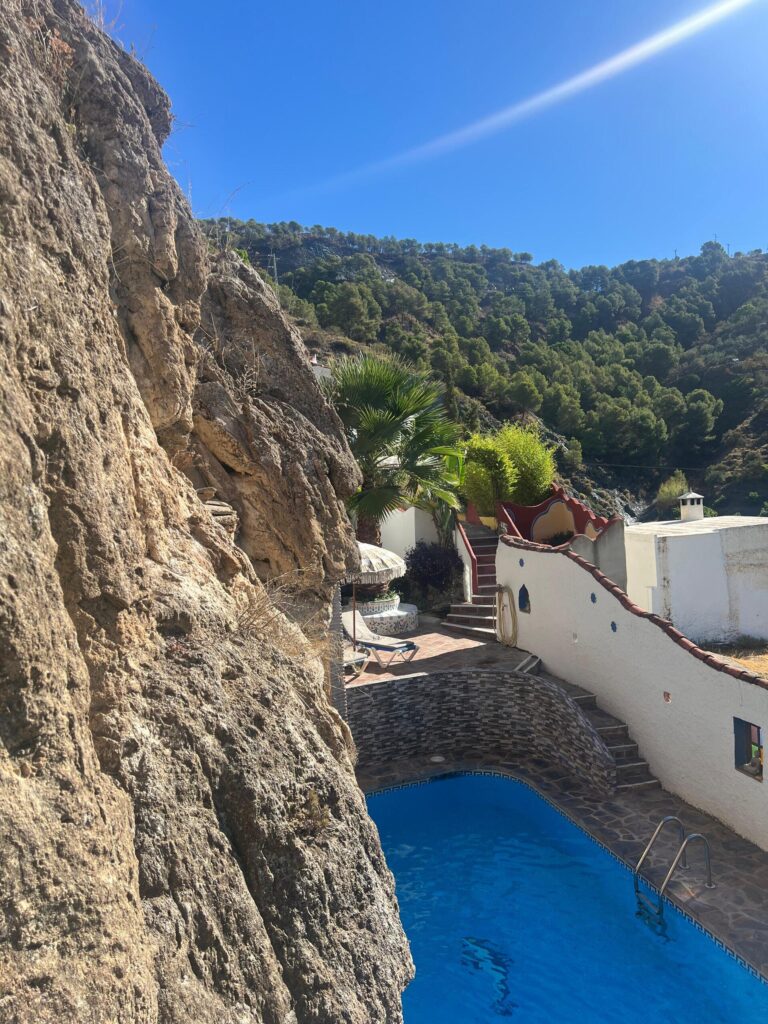 View from the cave of the outdoor pool carved into the mountainside at Molino del Rey retreat with blue skies and the Andalusian hills in the background