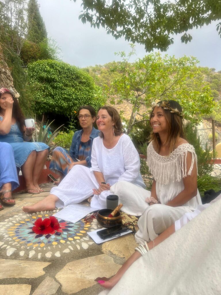 Somarising women's retreat - women gathered in a sacred sharing circle outdoors, sitting cross-legged on the ground with flowers and a Tibetan singing bowl in the centre
