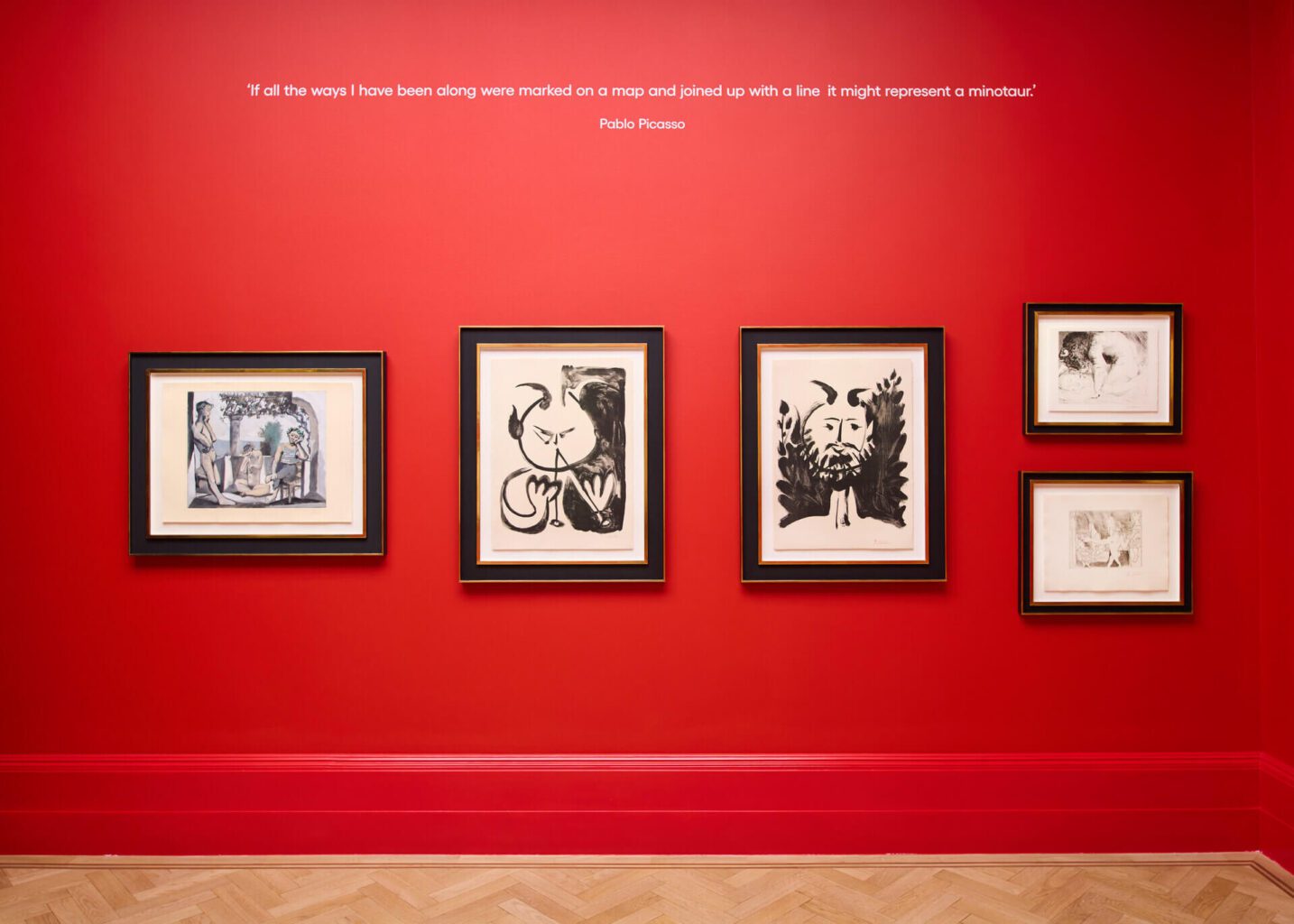 Gallery corridor featuring Picasso work, with striking red walls and framed portraits, part of Picasso: A Legacy Exhibition in London.
