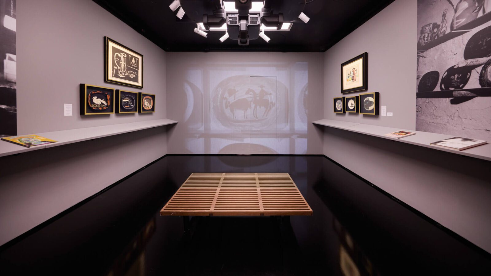 Exhibition space displaying Picasso's ceramic works and prints with Picasso on film projection under gallery lighting at Picasso: A Legacy, the free new Picasso exhibition in London.