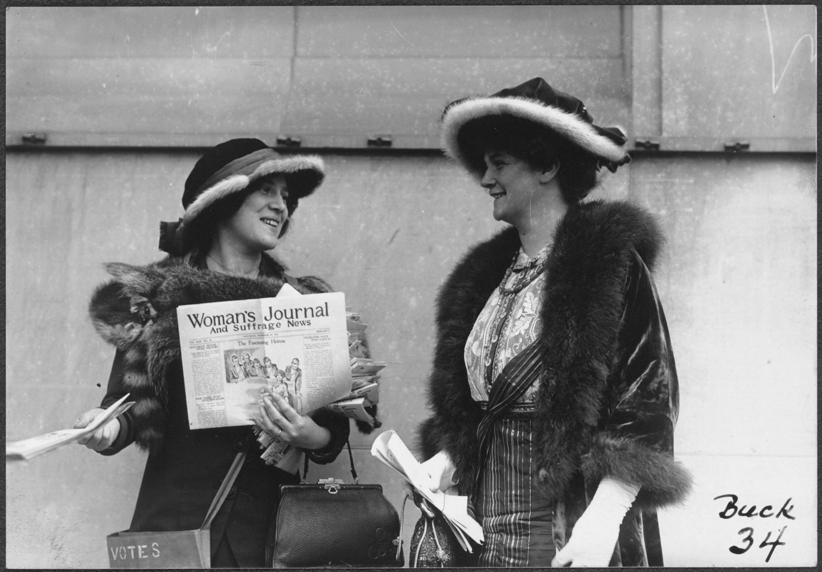Two women suffrage activists wearing early 20th-century clothing sell copies of the Woman's Journal and Suffrage News